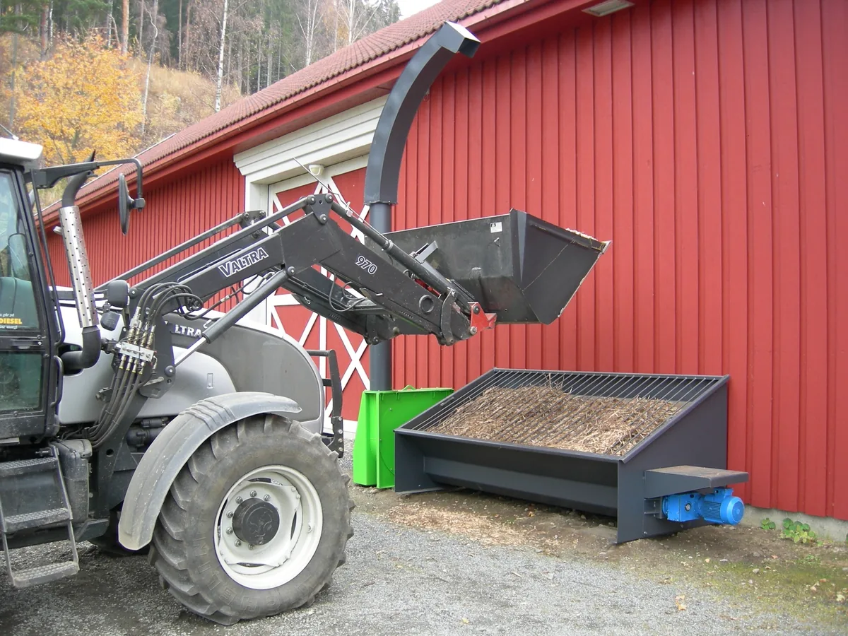 Traktor med skuff ved flistørka foran den røde låven på Eidsalm en høstdag.